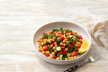 Healthy vegan salad with chickpeas, tomatoes, cucumbers, bell peppers and kale on light wooden background, space