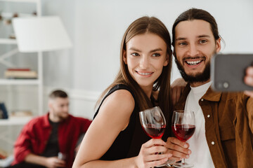 Image of friends taking selfie on mobile phone while drinking wine