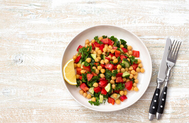 Healthy vegan salad with chickpeas, tomatoes, cucumbers, bell peppers and kale on light wooden background, flat lay, space	