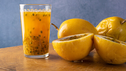 Passion fruit and a glass of juice on rustic wood, blue background, selective focus.