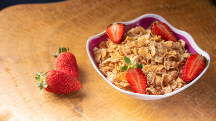 Breakfast cereal, corn flakes, strawberries in a bowl on rustic wood, selective focus.