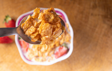Breakfast cereal, corn flakes, strawberries and milk, in the foreground a spoon with corn flakes and milk. selective focus.
