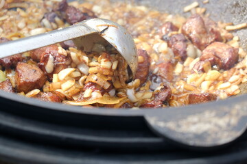 Cooking meat outdoors in cast-iron cauldron. Cooking meat on a fire. Food in a cauldron on a fire. Cooking food in nature on the cauldron.Uzbek pilaf in a huge cauldron