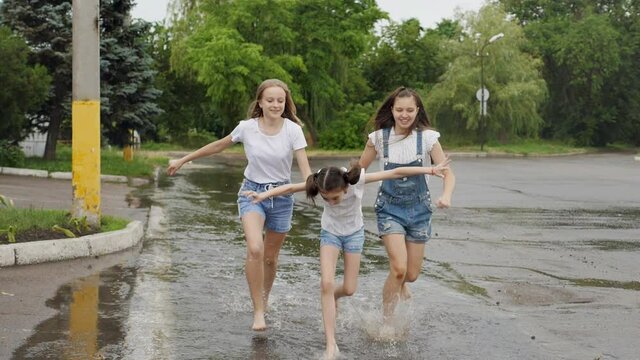 Teenage girls have fun running through puddles after the rain.