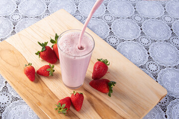 Putting strawberry juice in a glass on wood with strawberries around it, Top view.