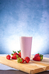 Strawberry juice in a glass on wood with strawberries around, blue gradient background, selective focus.
