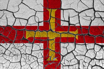 Flag of Guernsey on a cracked wall, dry ground	