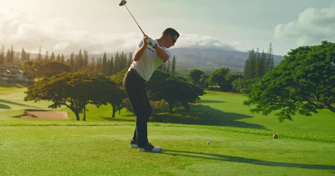Man swinging and hitting golf ball on beautiful golf course at sunrise, slow motion