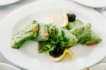 Spinach pancakes with red caviar in a white plate on the table. A delicious stylish dish. Serves dinner on a festive table. Food on festive table at wedding banquet.