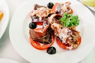 Gourmet salad in a white plate. Slices of cheese, tomato, lettuce. White plate on table. Food. Holiday.
