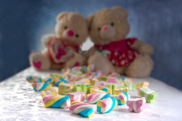 Colorful marshmallows in detail and defocused teddy bears in the background, blue gradient background, selective focus.