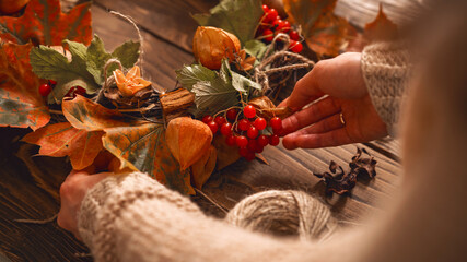 Making a wreath of autumn leaves and natural materials on rustic wooden boards.