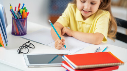 little girl writes in a notebook, does her homework, using a tablet computer