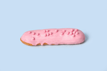Bright Eclair in pink glaze sprinkled with colorful pink jelly beans, balls. Isolated on a blue background.