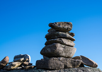 Stack of rocks on a boulder with smaller rocks to the side against a bright blue sky.