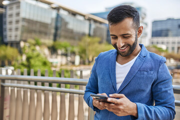 Portrait of smiling Indian arabic business man typing on mobile phone in city