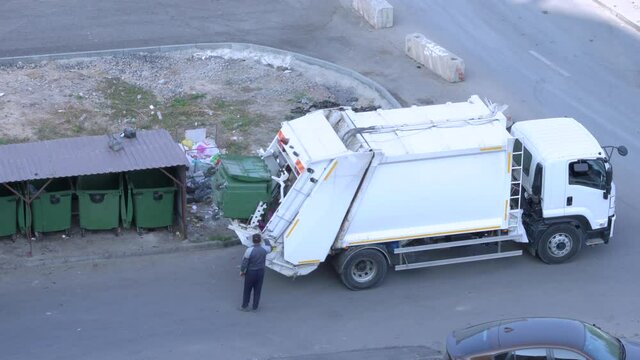 Employees of communal services collect municipal waste from large street trash bins in garbage truck to transport it to solid waste treatment facility, such as landfill or transfer station.
