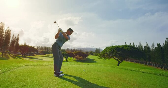Man playing golf at sunrise, swinging and hitting golf ball, slow motion