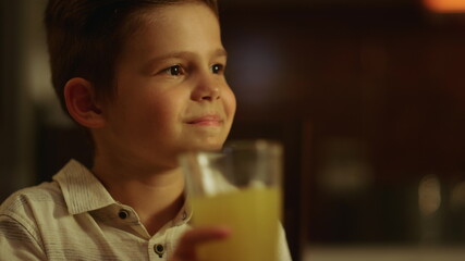 Boy sitting at dining table. Smiling child holding glass of juice in hand