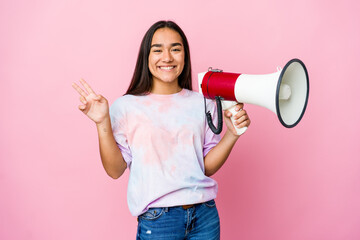 Young asian woman holding a megaphone isolated on pink background joyful and carefree showing a peace symbol with fingers.