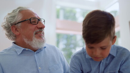 Smiling grandfather looking at grandson. Joyful boy sitting on grandparent laps