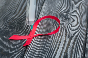 Red Ribbon Symbol for World AIDS Day. A medical syringe is inserted into it. On black pine boards.