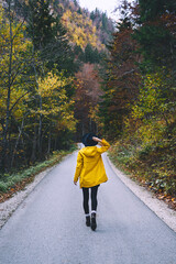 Woman in yellow raincoat walking on road in autumn forest.