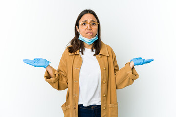 Young latin woman wearing a mask to protect from covid isolated on white background confused and...