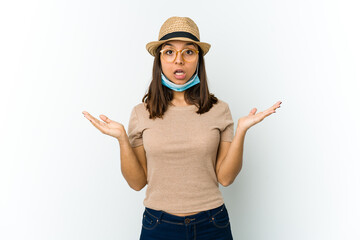 Young latin woman wearing hat and mask to protect from covid isolated on white background surprised and shocked.