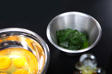 Ingredients for making homemade pasta with spinach. Spinach and eggs in a metal dish.Top view.