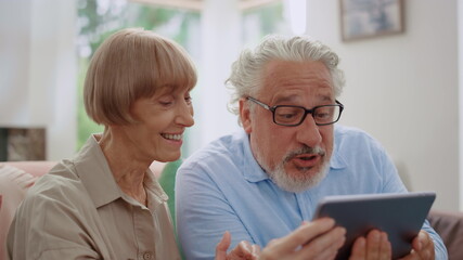 Grandmother and grandfather talking by video call on tablet with grandchildren