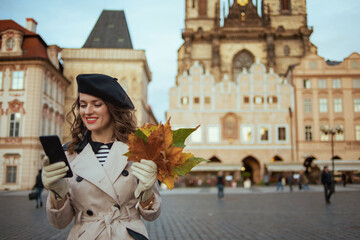 smiling female in beige trench coat and beret using phone app