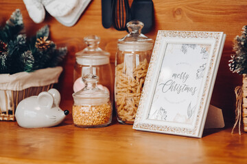 Close-up of containers of cereals, salt cellar in shape of New Year s symbol mouse and photo frame with Merry Christmas text.