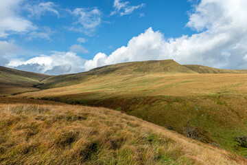 Naklejka premium A scenic view of a mountain valley with green slopes under a beautiful blue sky and some white clouds