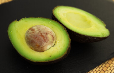 ripe halved avocado with bone on black stone board