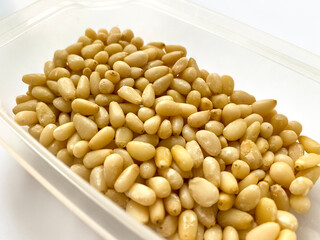 Peeled kernels of pine nuts in a plastic cup on a light background. close-up