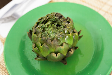 cooked whole artichoke on a green plate