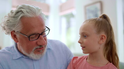 Grandfather talking with granddaughter at home. Girl sitting on grandfather laps