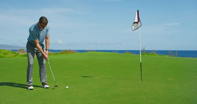 Man playing golf on beautiful course by the ocean, putting on the green into the hole