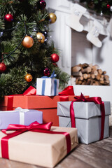 Selective focus of gift boxes near pine and fireplace with christmas stockings