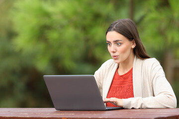 Surprised woman checking laptop in a park