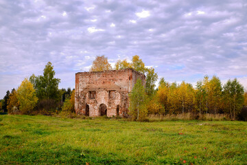 The ruins of an old red brick building surrounded by trees, autumn day.