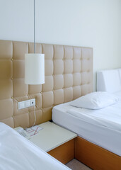 Sunny room in a hotel in light colors with two beds, nightstand and a lamp
