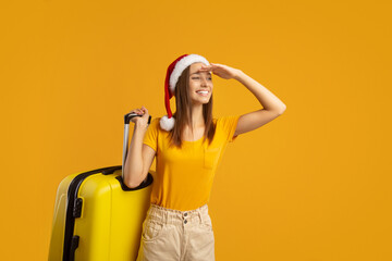 Smiling woman traveller with Santa hat carrying suitcase