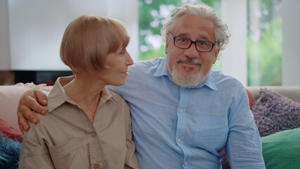 Senior woman looking at man. Mature couple sitting on couch in living room