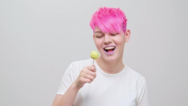 Young beautiful girl with a short haircut and pink hair. A homosexual lesbian model poses on a white background in the studio.
