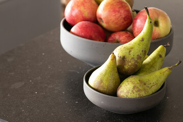 Apples and pears in gray bowls on a dark countertop