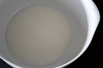 Sugar inside a white bowl in a dark background, following a cup cake recipe