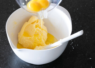 Mixing eggs with butter sugar creamy dough in a white bowl for cup cakes, following a recipe