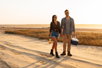 Couple holding hands together while strolling with bear and cooler bag